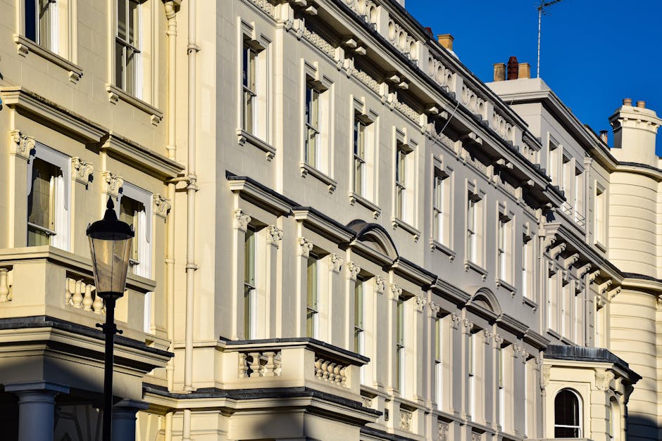 Photograph of a historic, cream-colored Victorian-style building under bright blue sky, featuring large rectangular windows with white frames, decorative window ledges, ornate cornices, and detailed a